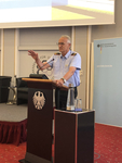 Mann in Uniformhemd spricht an Rednerpult mit Bundesadler-Emblem. Im Hintergrund ein Banner der Bundesakademie für Sicherheitspolitik.