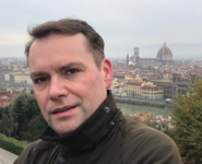 Porträt eines lächelnden Mannes vor der Kathedrale von Florenz (Dom) und der Stadtkulisse mit dem Arno.