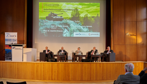 Eine Podiumsdiskussion über Sicherheitspolitik und Zeitenwende mit fünf Sprechern auf der Bühne und einer Präsentation im Hintergrund.