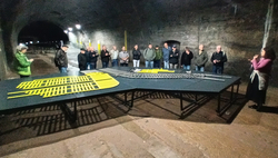 Gruppe in dunklem Tunnel betrachtet Modellgleisanlage auf Tisch; eine Frau präsentiert.