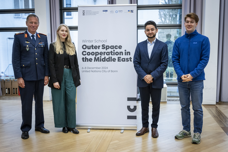 Gruppenfoto von vier Personen: einem Mann in Uniform, einer Frau und zwei jungen Männern, vor einem Raumfahrt-Winterschul-Banner.